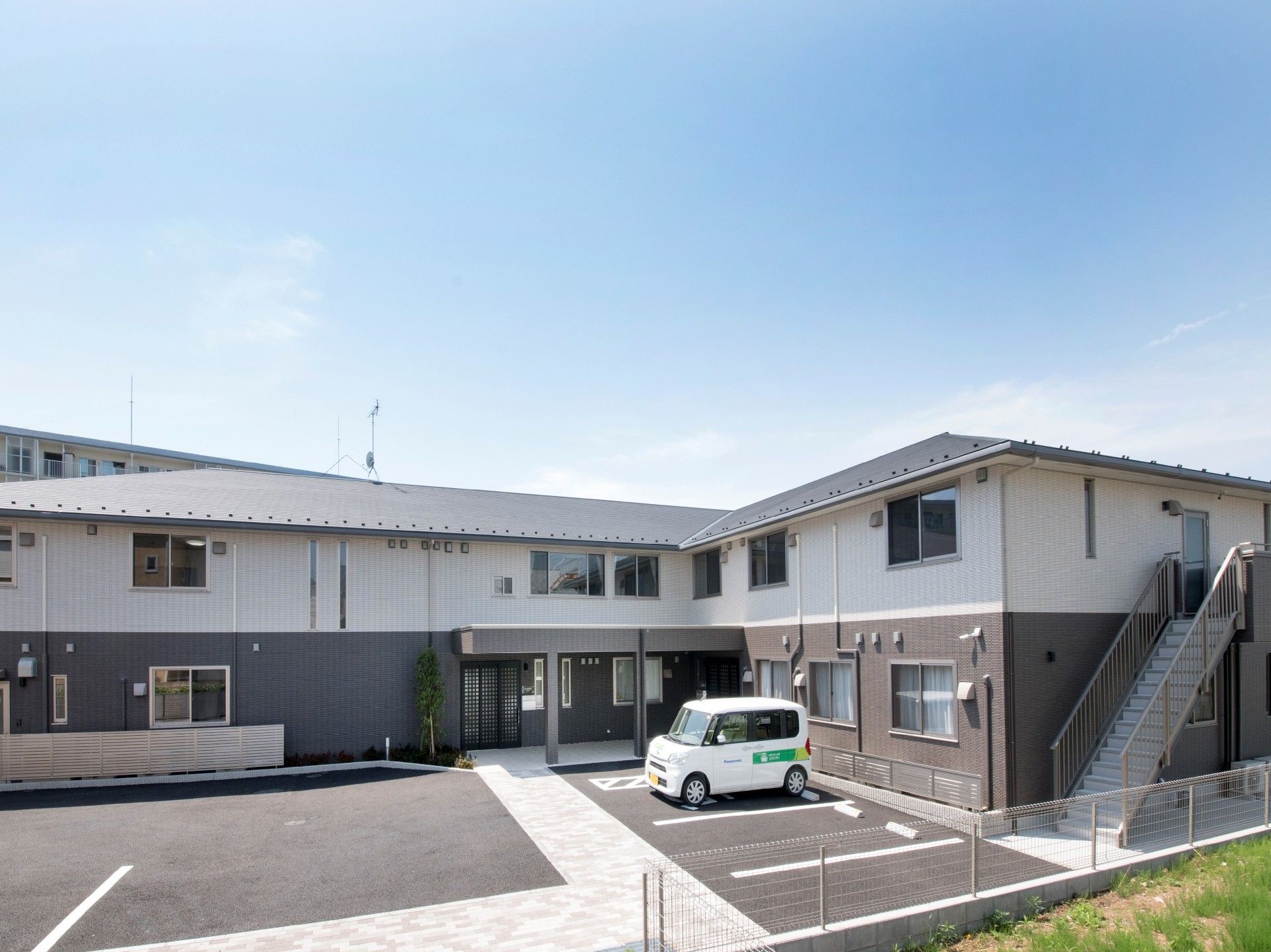 屋外階段が付いた建物は2階建てでシンプルなデザイン。駐車スペースには白い車が止まっている。