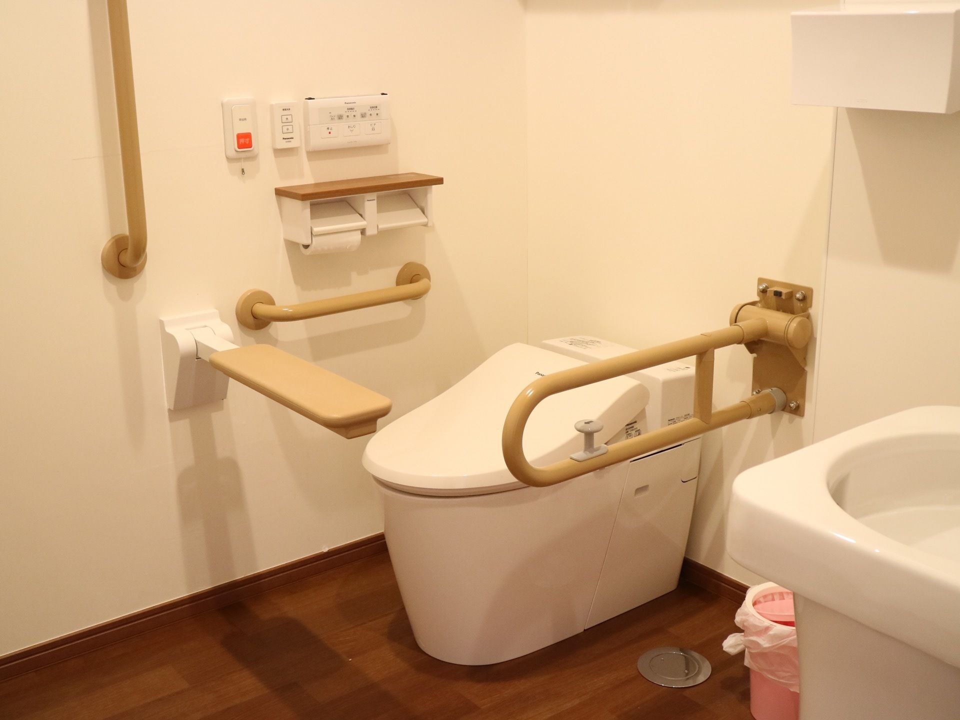 トイレには温水洗浄便座が完備されている。壁や便器周辺には、明るいブラウン系の介助バーや手すりがある。