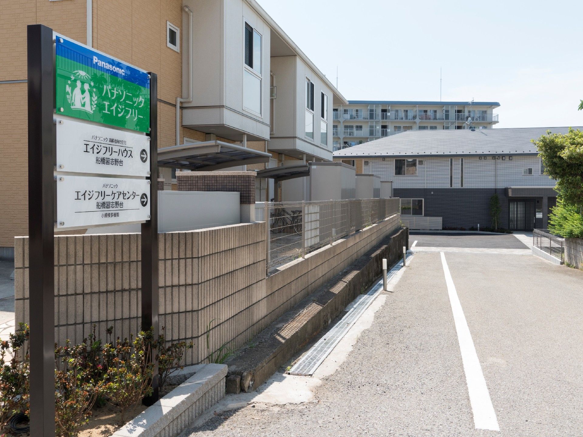住宅と併設事業所の看板が設置されている。まっすぐな道路の突き当りに2階建ての建物が見える。