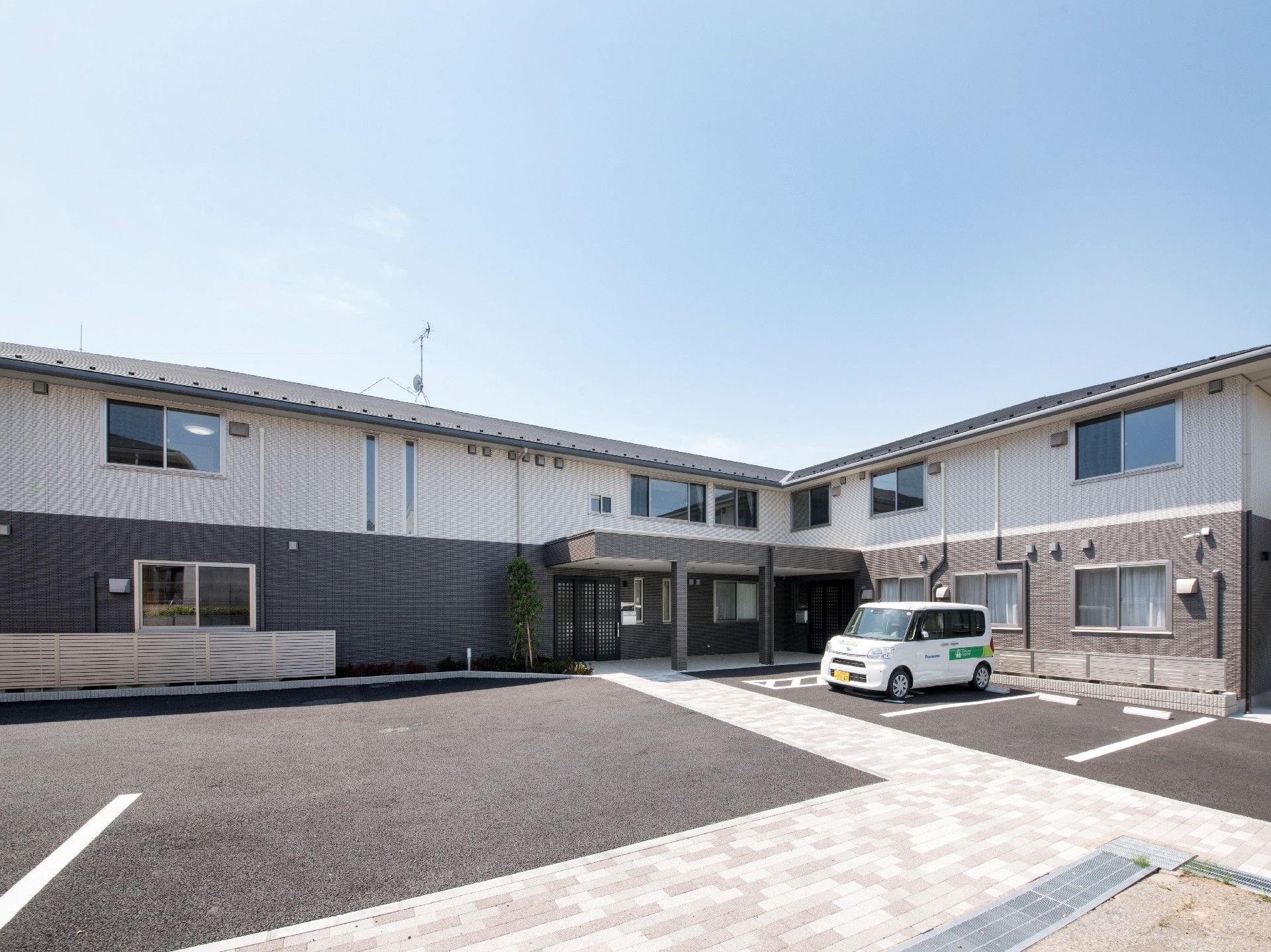 エル字型の２階建ての建物はモノトーン。玄関は自動ドアで、駐車所が広い。