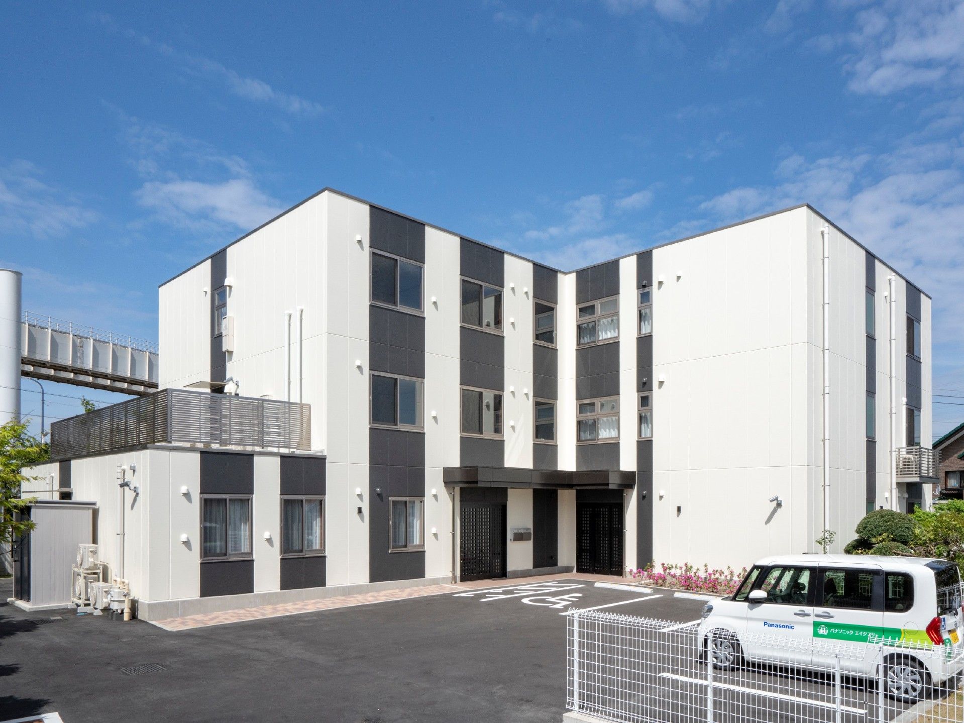 白をメインとした3階建ての建物には黒いストライプが縦に入り、駐車スペースもある。