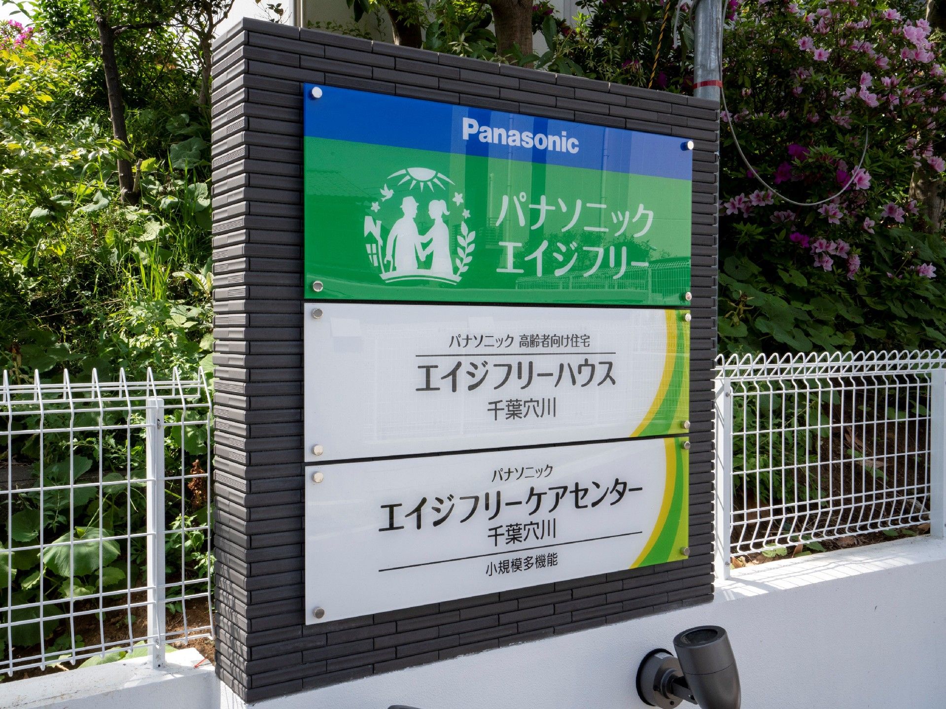 白いフェンスには住宅と併設事業所の名前が書かれたプレートが貼られている。