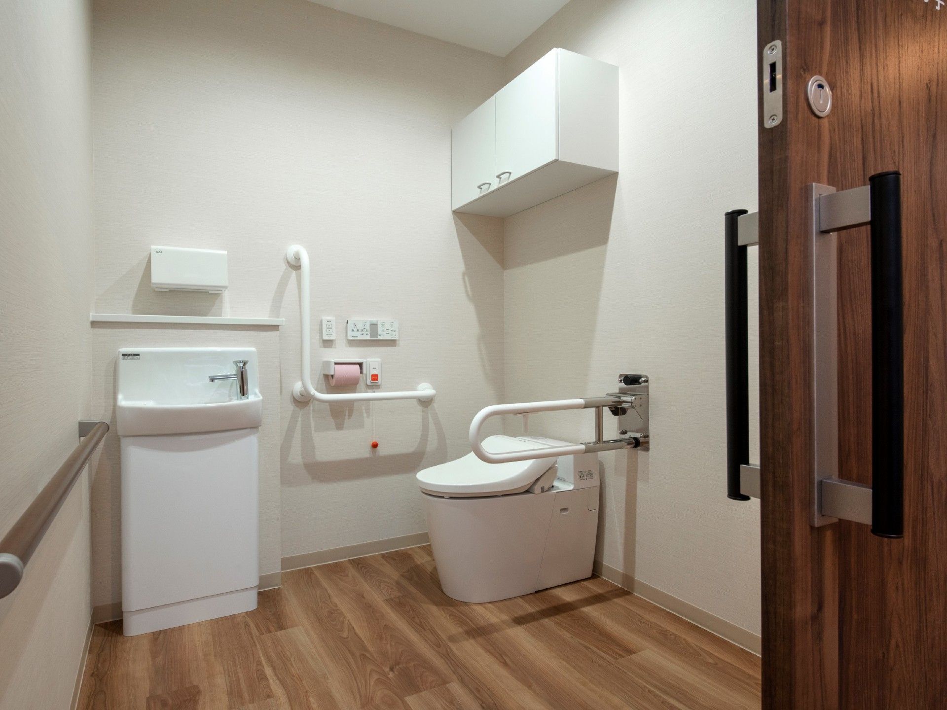 引き戸が付いたトイレは広く、壁にエル字型の手すりと呼び出しボタン、棚が付き、可動式の手すりも設置されている。