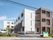 白とブラウンの3階建ての建物の周りには緑も多く、玄関には屋根がある。