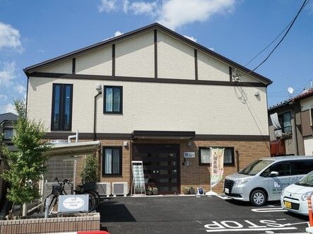 駐車場が付いた２階建ての建物は三角屋根が付き、1階と2階の外壁の色が異なる。アットホームな雰囲気。