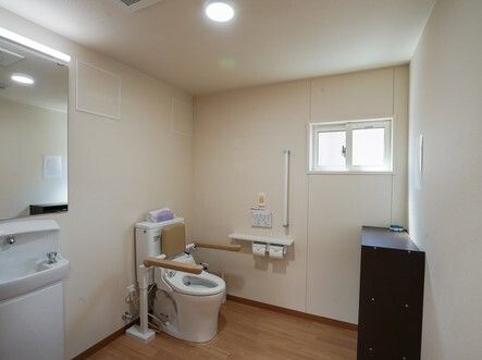 手すりや背もたれが付いた便座が設置されたトイレは広く、壁には手すりが付き、オレンジの呼び出しボタンもある。