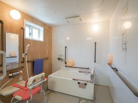 ダークブラウンの手すりが付いた浴室内には一人用の浴槽が設置され、シャワーの前にはシャワーチェアが置かれている。