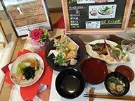 陶器の皿に盛られた天ぷらや焼き魚など豪華な食事内容。桜の花をあしらったランチョンマットが敷かれている。