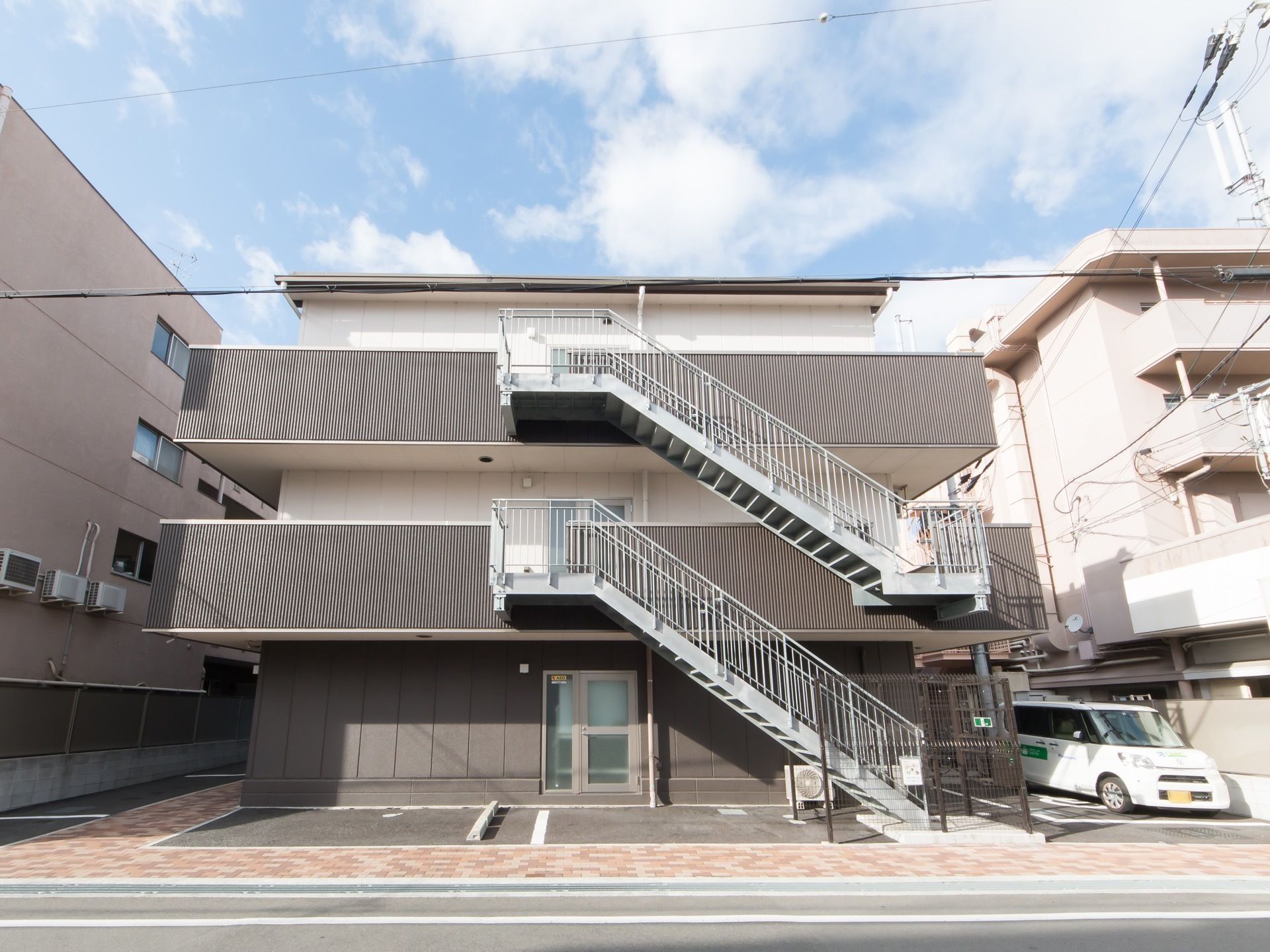 ３階建ての建物で、周囲に巡らしたベランダから外階段が続いている。駐車スペースが３台分ある。出入口が設けられている。