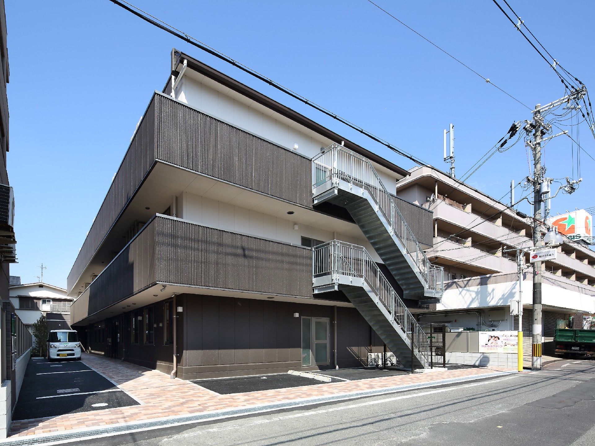 グレーと白の建物は3階建てで、ベランダや駐車場も設置されている。