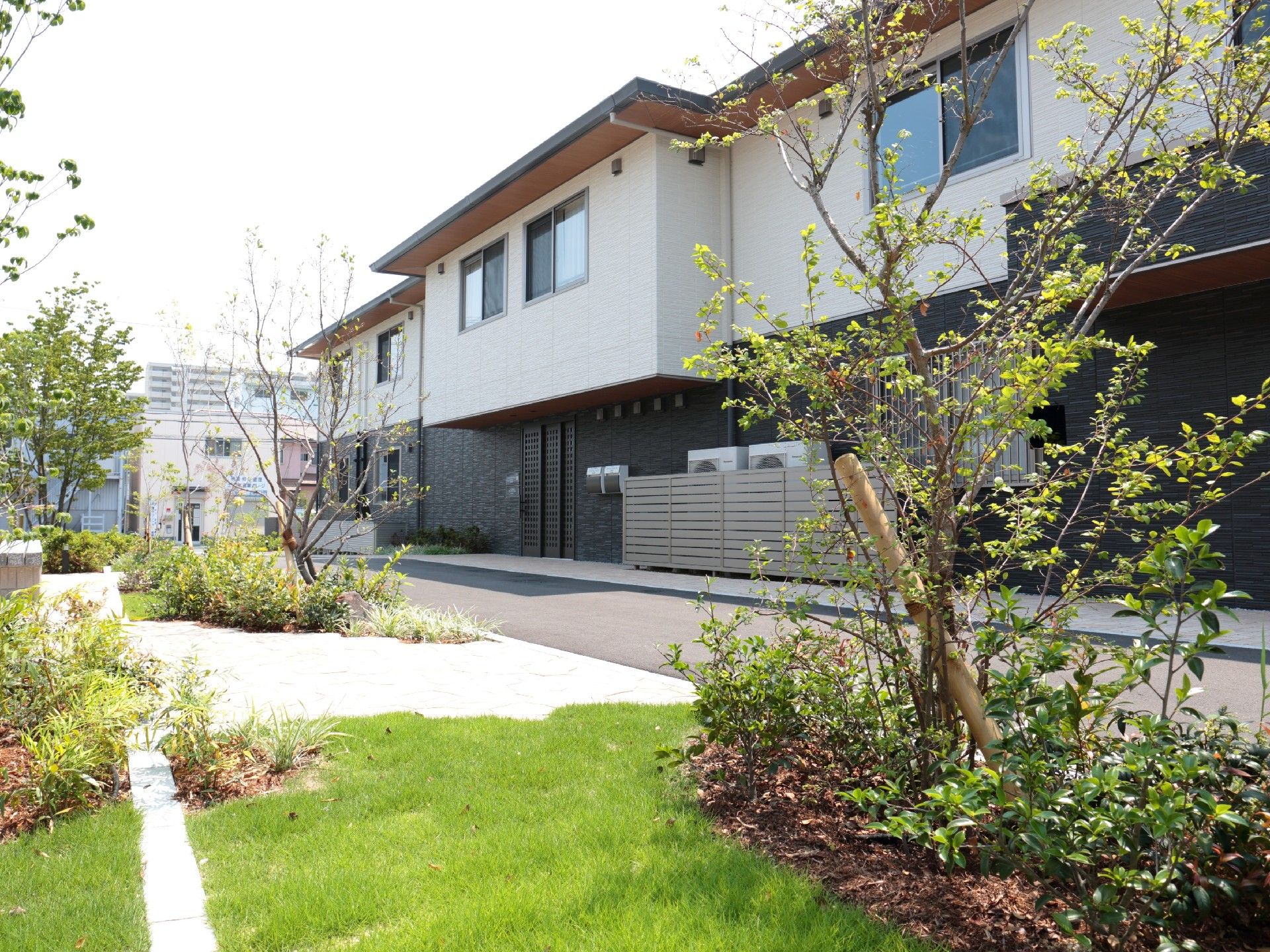 手前には芝生が敷かれ気が植えられた庭があり、奥には2階建ての建物が見える。