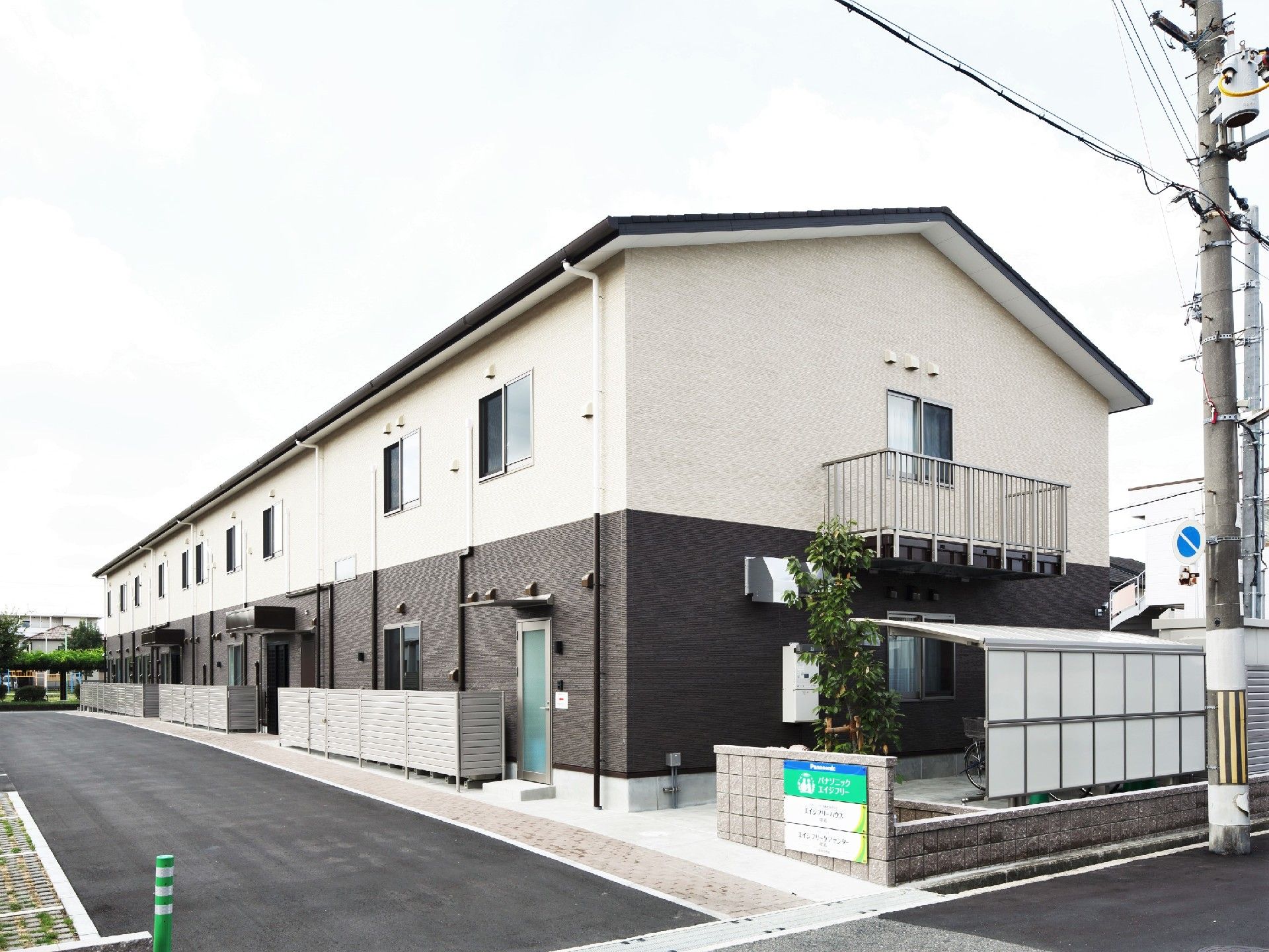 道路の面した２階建ての建物には駐輪スペースが付き、門には住宅と併設事業所の名前が書かれたプレートが貼られている。
