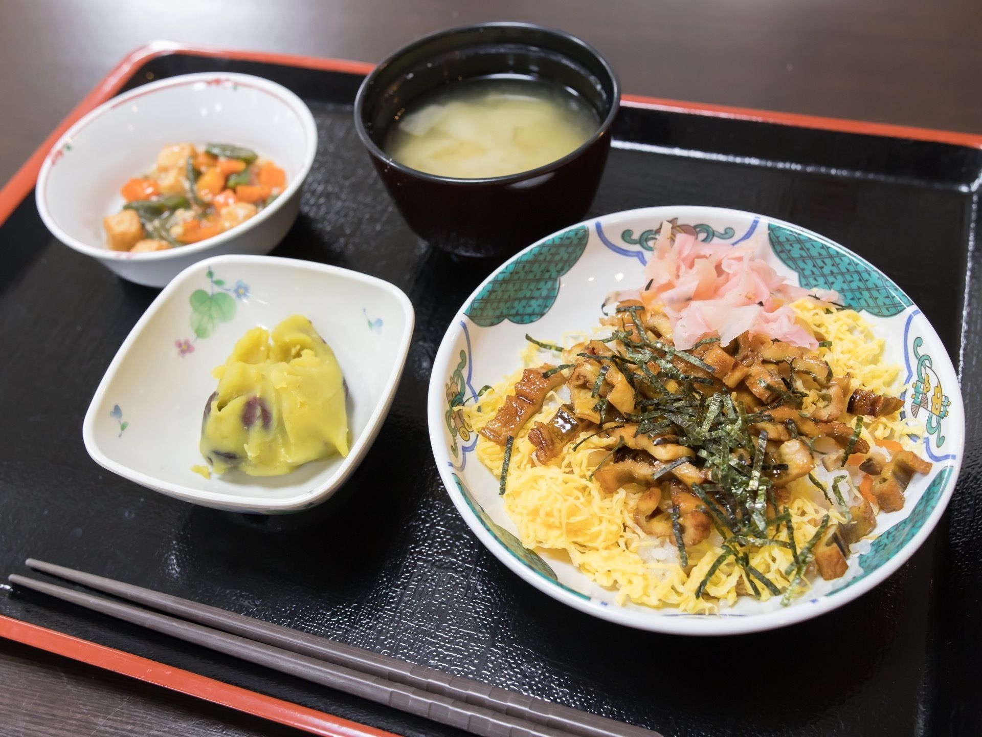 ある日の献立である。黒いプレートに主食や汁物、デザートなどが器に盛られてお箸とともに並べられている。