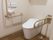温水洗浄便座が完備されたトイレである。壁には緊急呼び出しブザーやL字型手すり、可動式手すりがある。