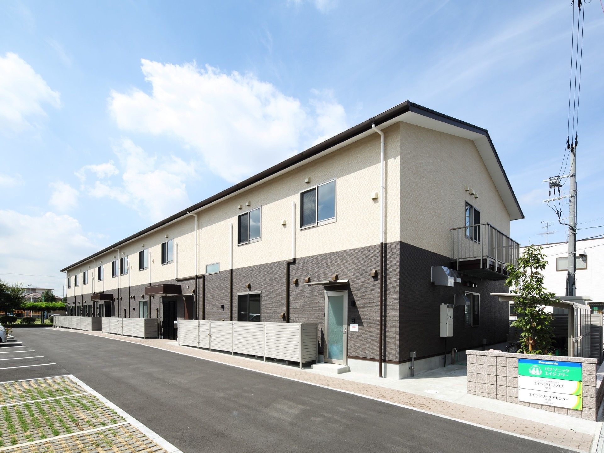 横に長い長方形の建物は2階建てで、1階がダークグレー。駐輪スペースもある。