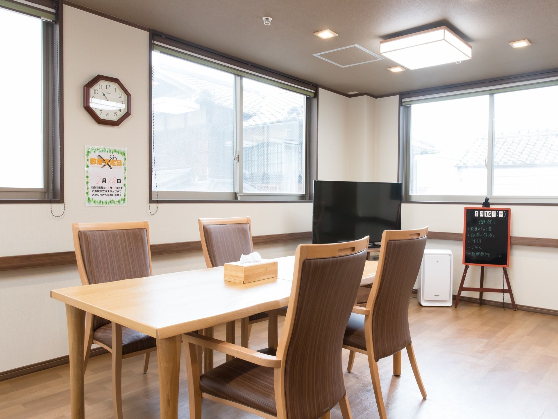 複数の窓がある明るい食堂で、フロアの隅にはテレビが１台設置されている。食卓の上には、箱ティッシュが用意されている。