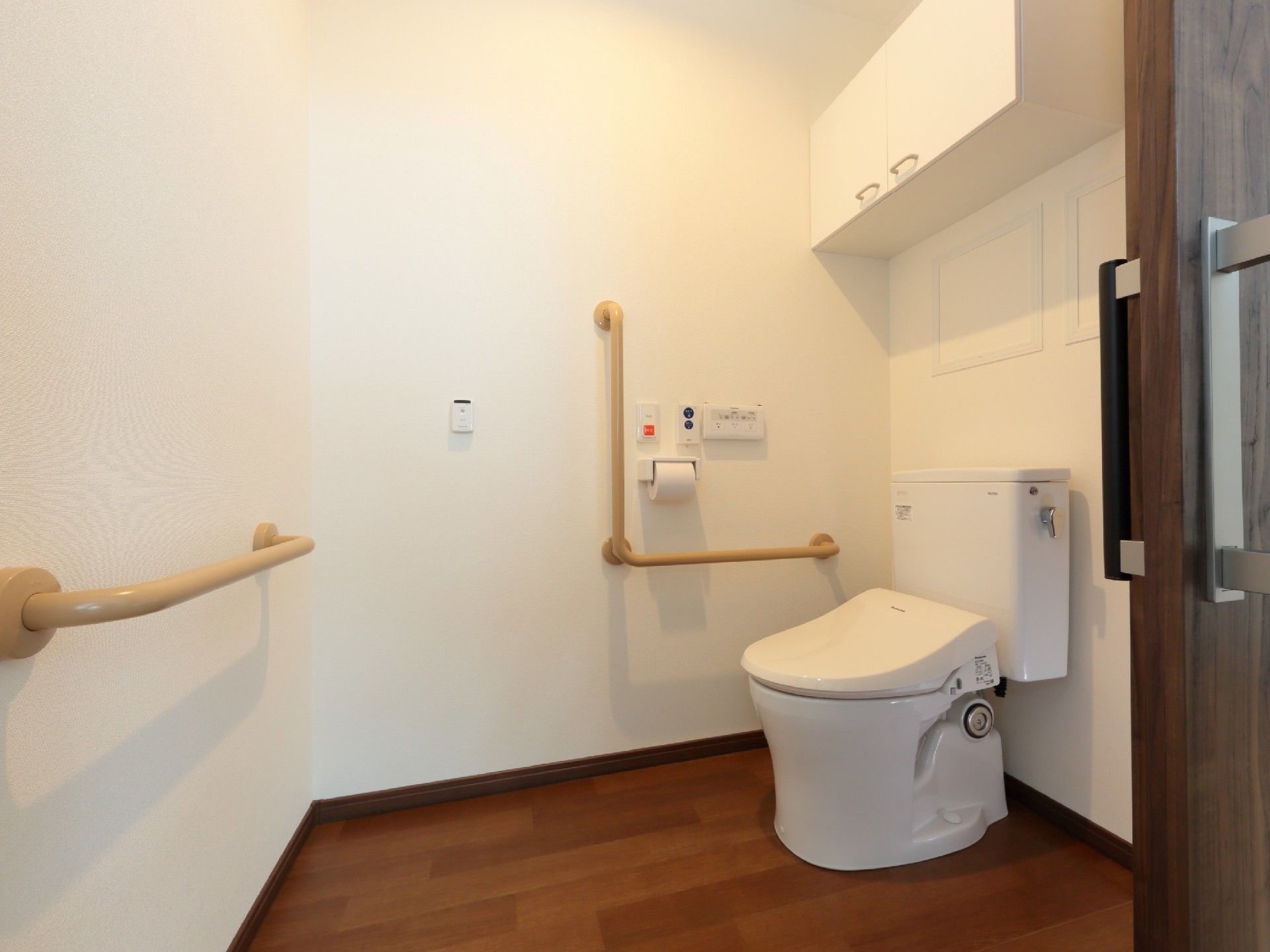 広いトイレには大きな収納棚が付き、壁には複数の手すりと呼び出しボタンが付いている。