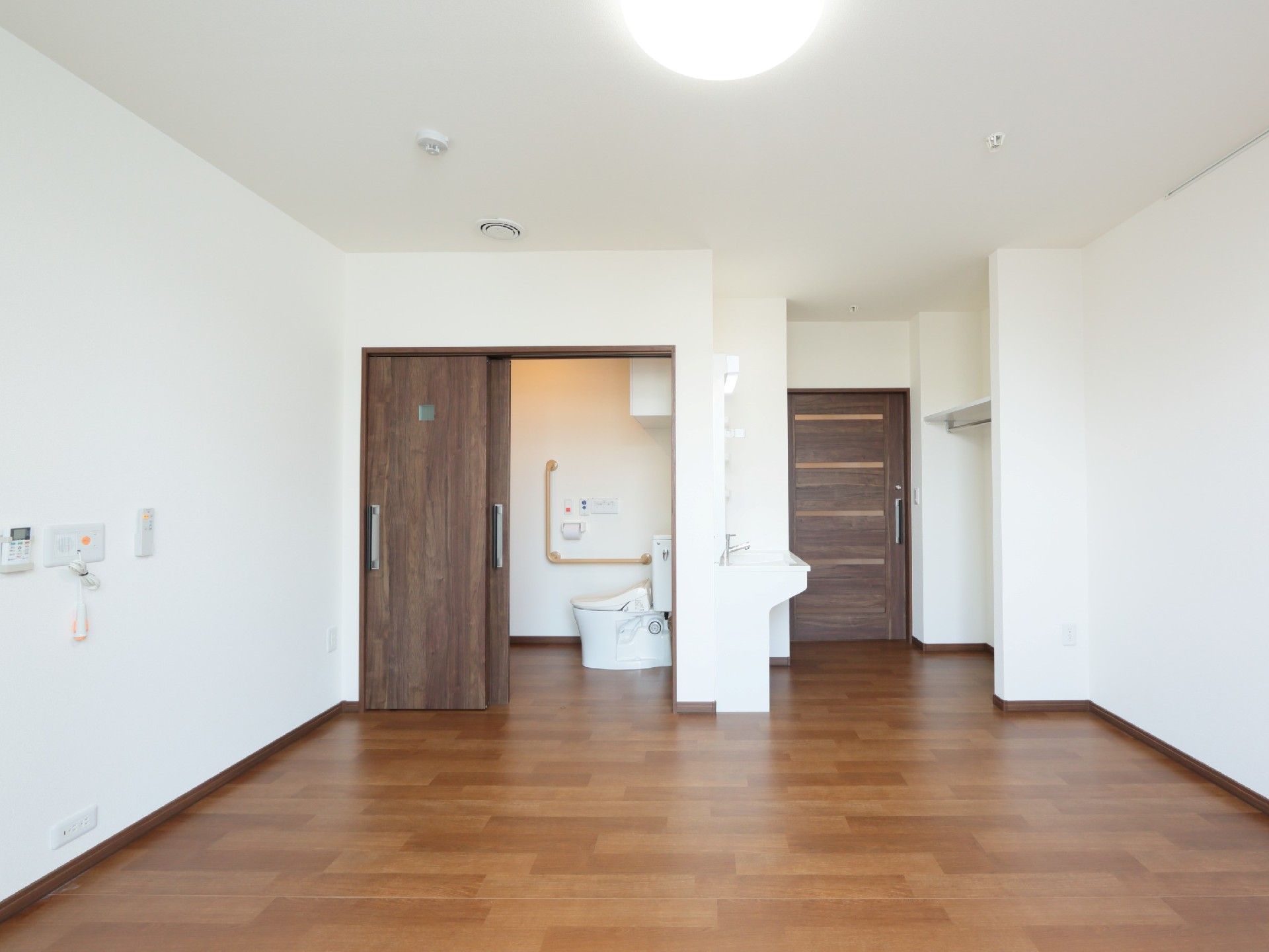 白い壁には緊急通報装置が付き、トイレは引き戸、洗面所もある居室。家具などはまだ置かれていない。