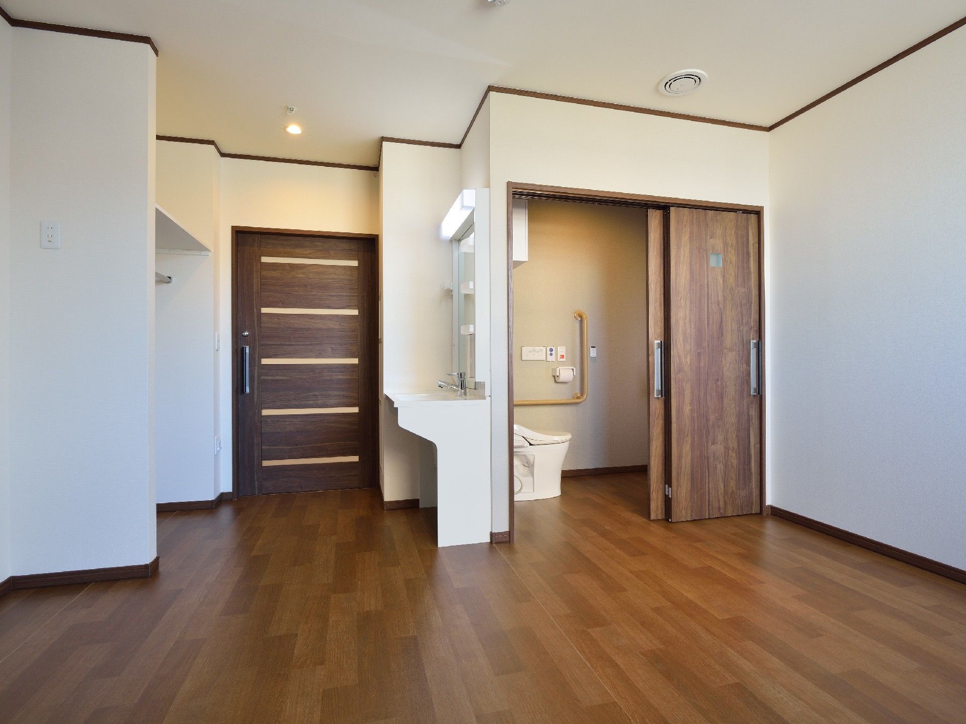 フローリングのシンプルな居室。トイレや洗面所、扉のない収納スペースなどが付いている。