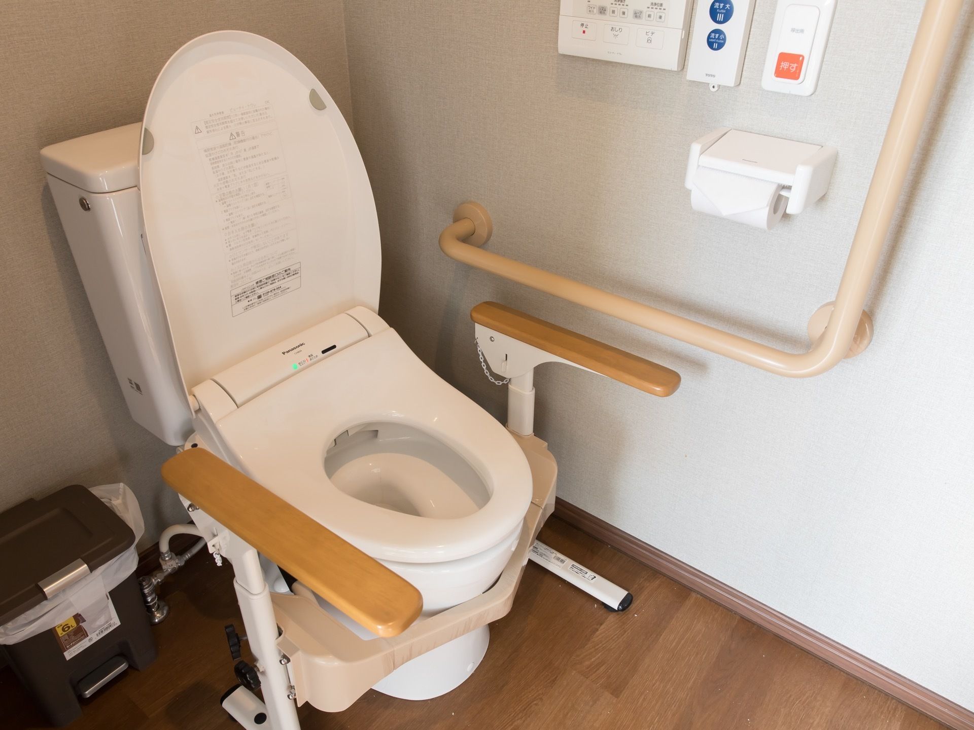 温水洗浄便座が採用されたトイレである。可動式のひじ掛けが設置されており、立ち座りの際に体を支えることができる。