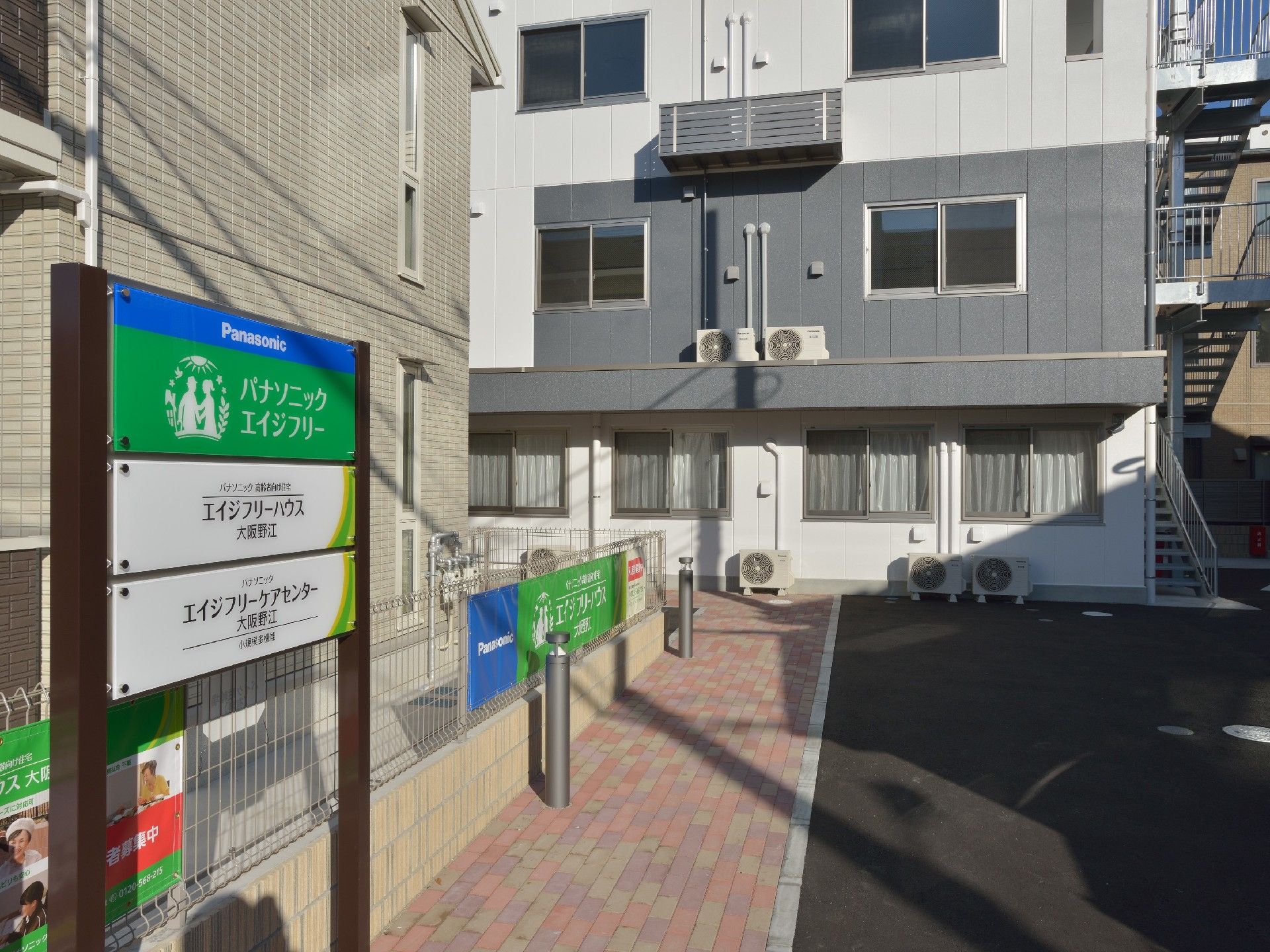 4階建ての建物に続くアプローチのわきには白とグリーン、青で統一された看板が設置されている。
