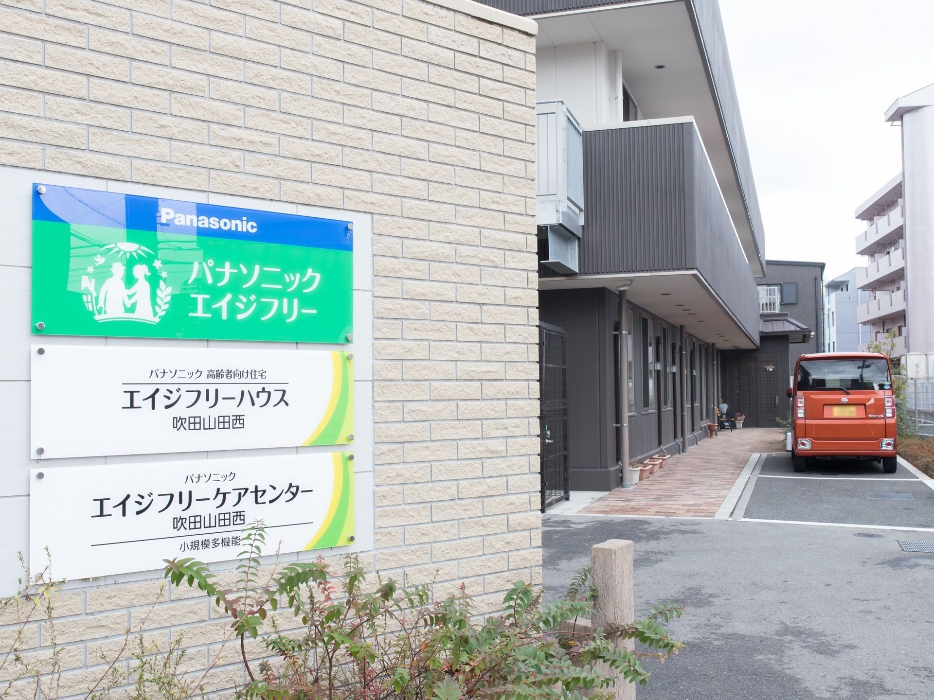 白とグレーにデザインされた施設である。出入口には、看板が設置されている。白線が引かれた、駐車場もある。