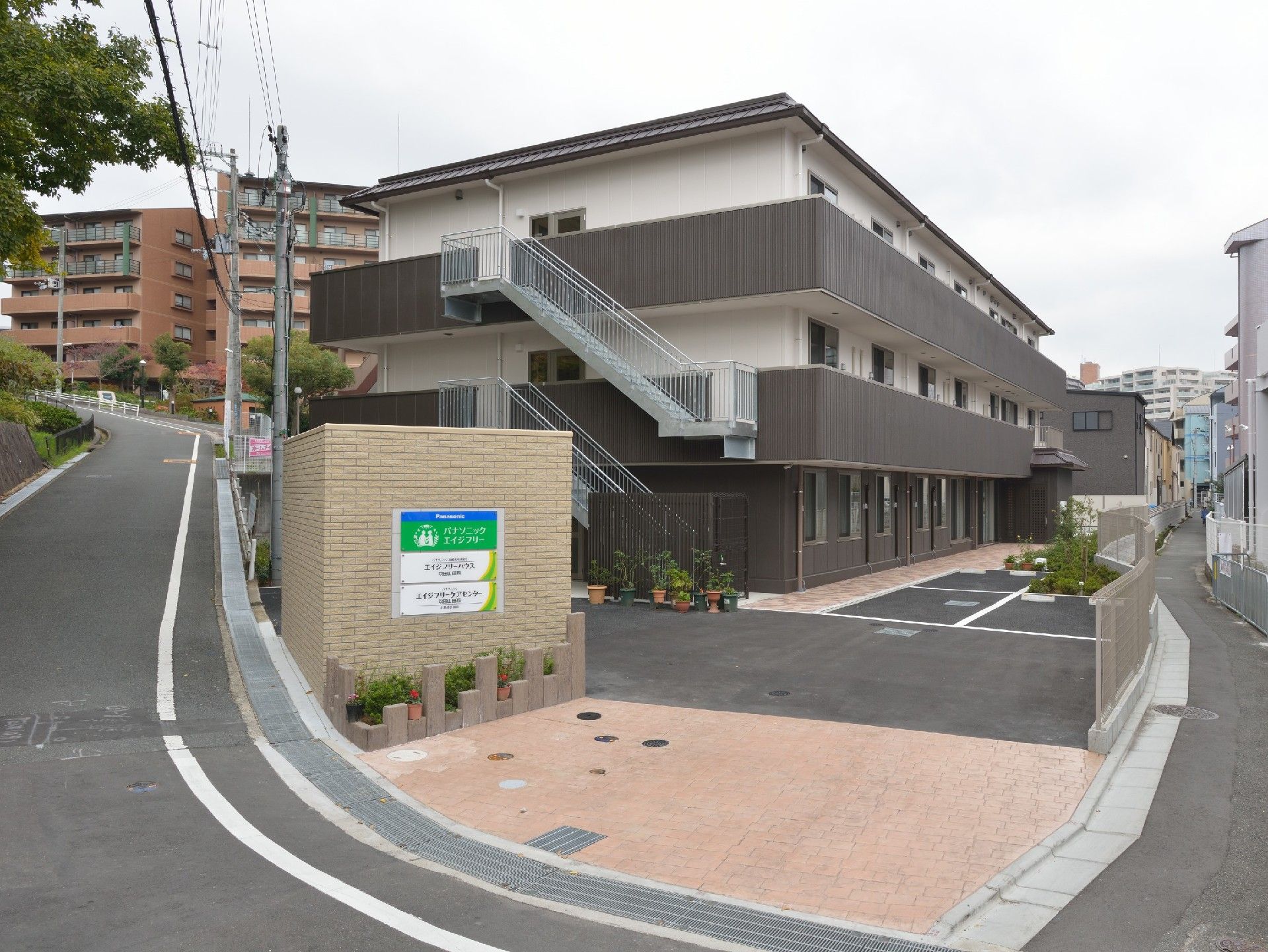 横に長い長方形の建物は３階建てで屋外階段やベランダ付き。駐車スペースもある。
