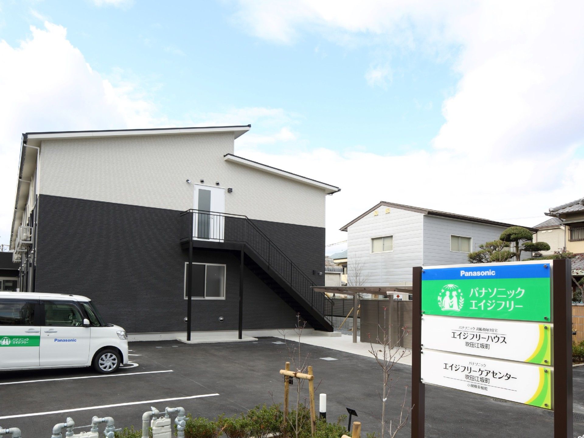 白とグレーの2階建て他の建物。側面には屋外階段があり、広い駐輪場もある。
