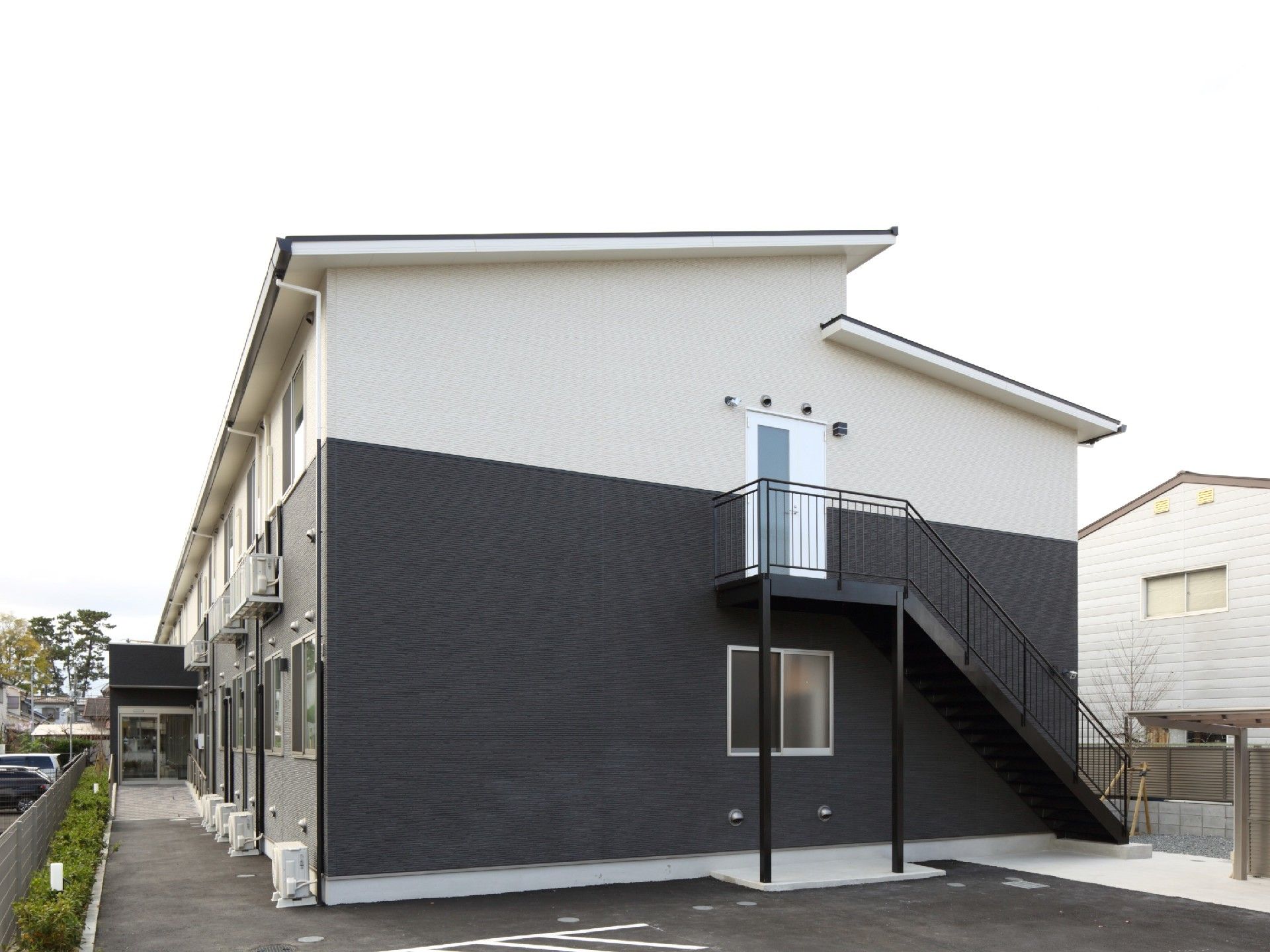 屋外階段が付いた建物は2階建てでシンプルなデザイン。広い駐車スペースもある。