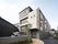 4階建ての建物の玄関部分は屋根が付き、玄関に続くアプローチ周辺には木が植えられている。。