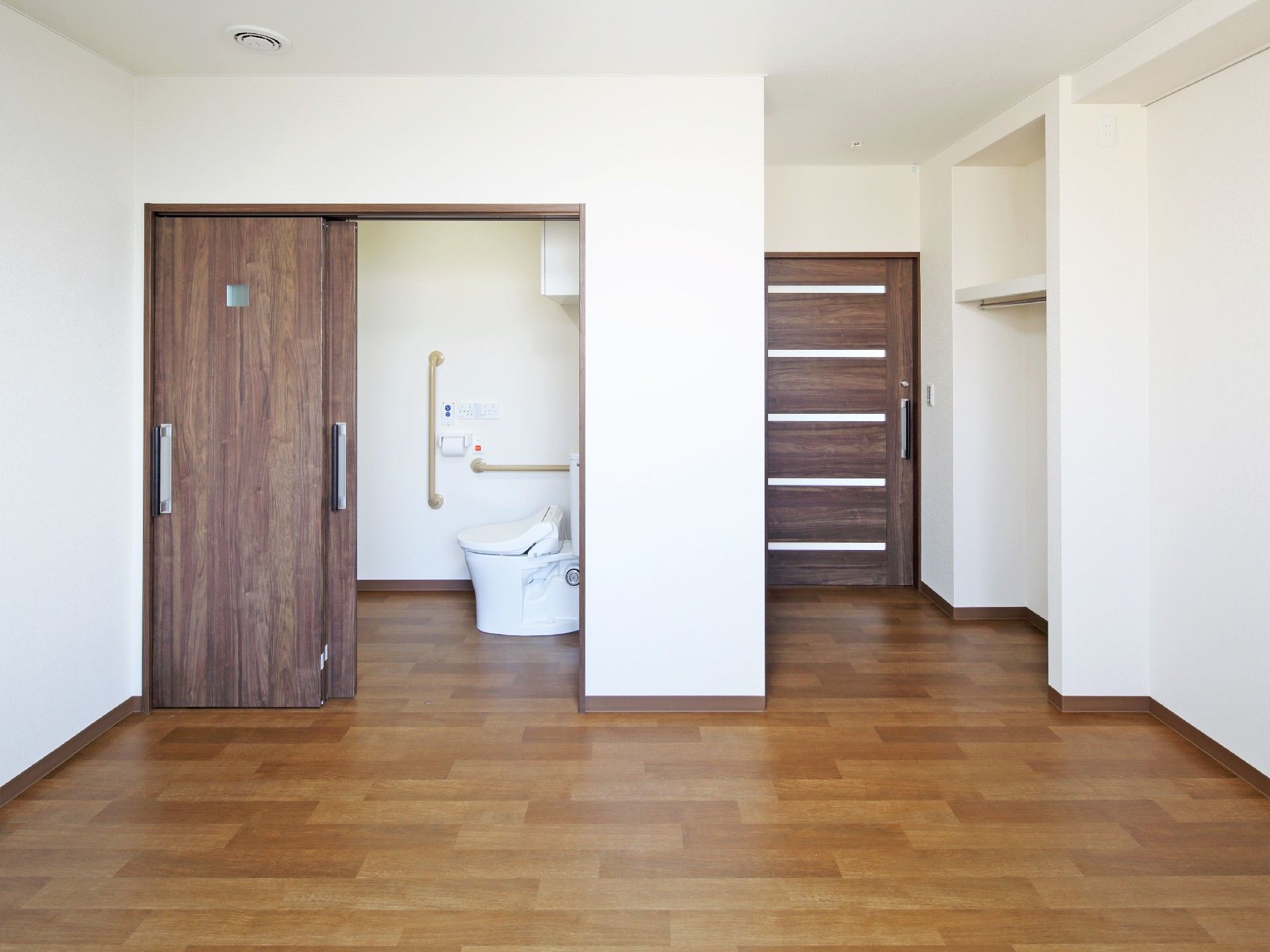 トイレや洗面所が付いたシンプルな居室は介護対応型のデザイン。壁には棚がある。