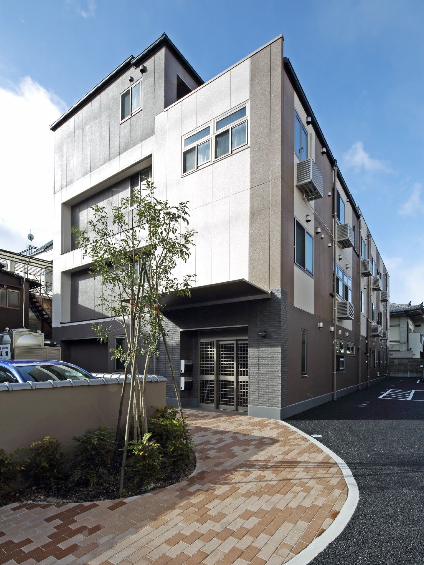 4階建ての建物に続くアプローチのわきには緑が植えられ、駐車場も設置されている。