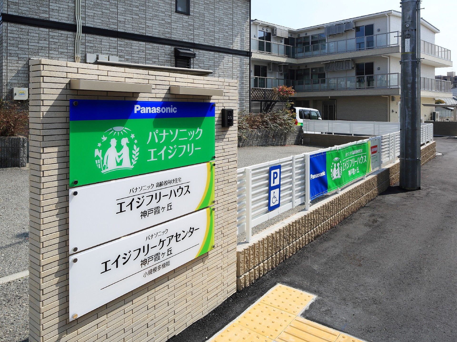 門には住宅と併設事業所の名前が書かれたプレートが貼られていて、建物周辺には白いフェンスがある。