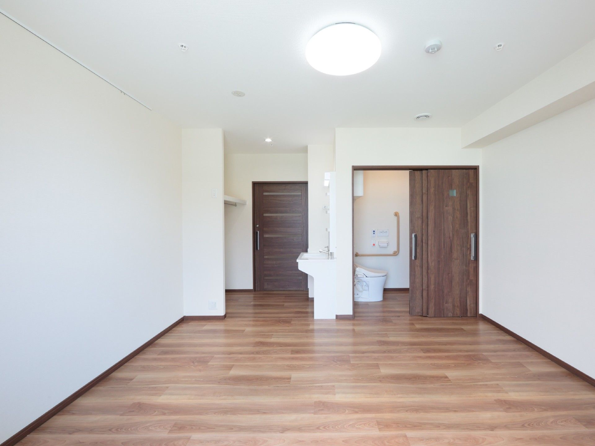 フローリングのシンプルな居室。トイレや洗面所、照明が付いている。
