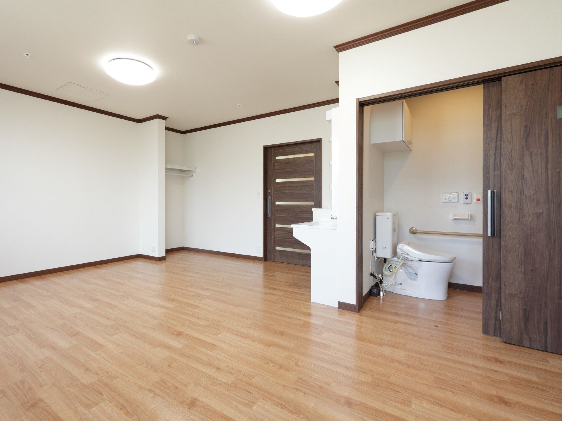 トイレには手すりが付き、洗面所や棚があるフローリングの広い居室。