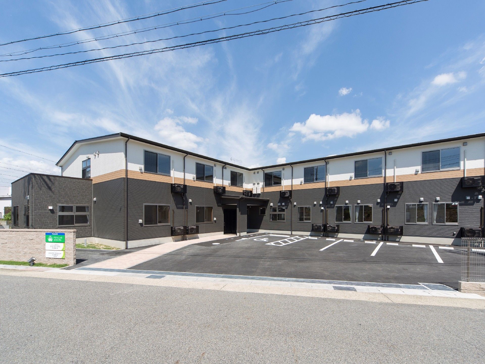 2階建ての建物。1階部分はブラウン、2階部分は白で、駐車スペースや看板もある。