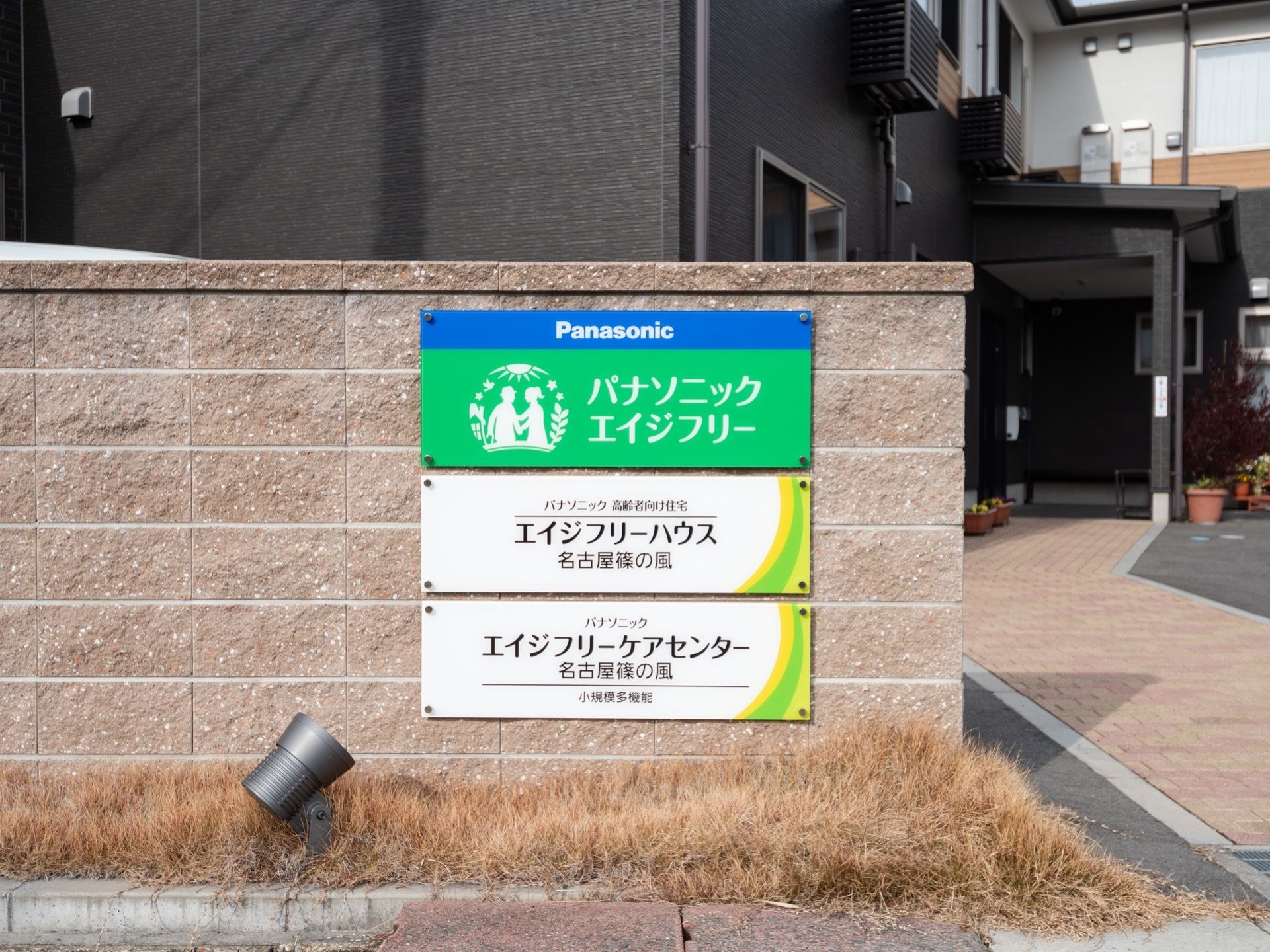 施設の敷地入り口に設置された看板である。ブロック塀に、3枚に分けて事業者名と高齢者向け住宅、ケアセンターである旨が記載されている。