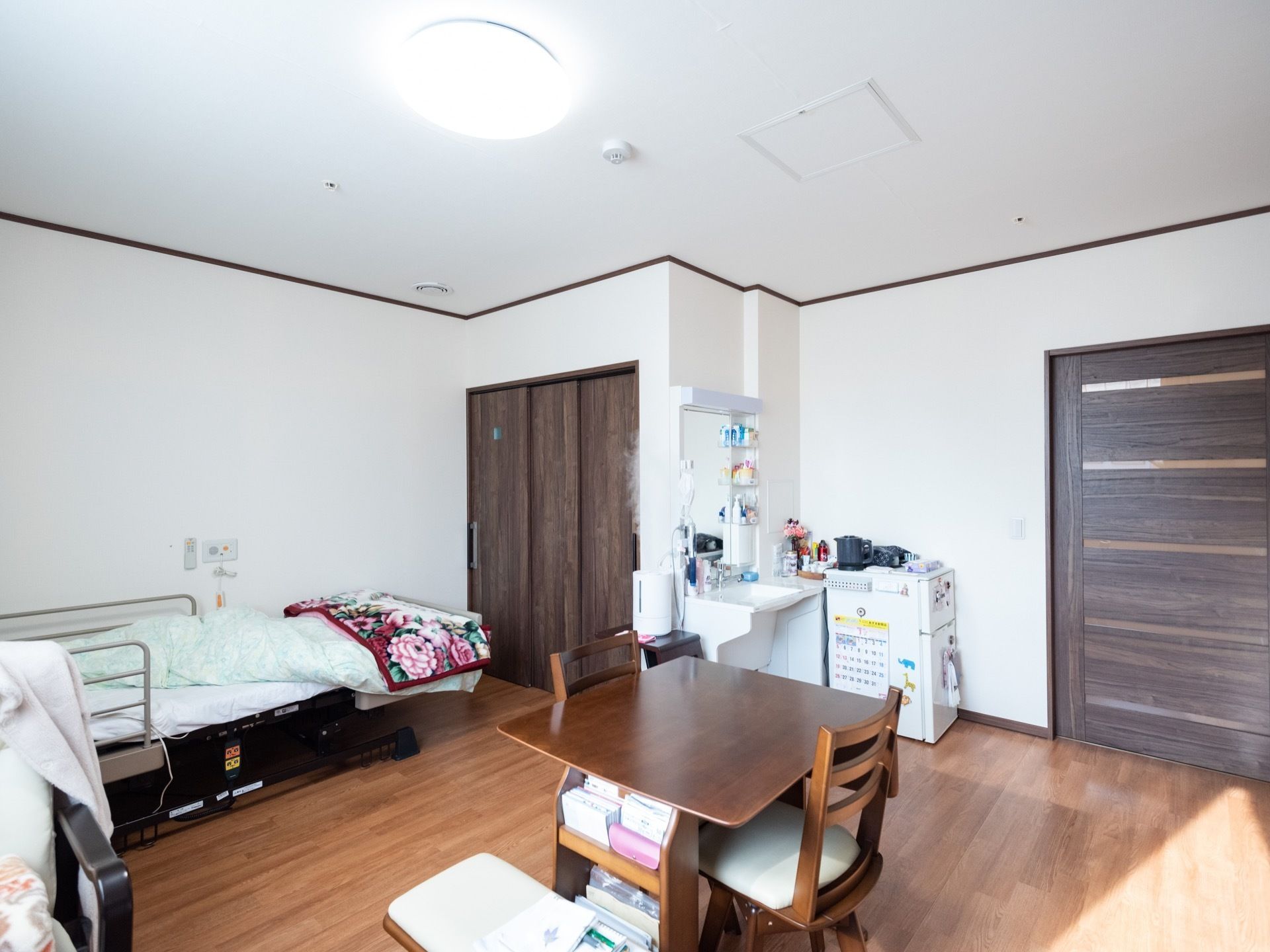 壁と天井が白で統一された、きれいな部屋である。ベッドが置かれ、収納や洗面台が設置されている。中央に小さなテーブルと椅子が置かれている。