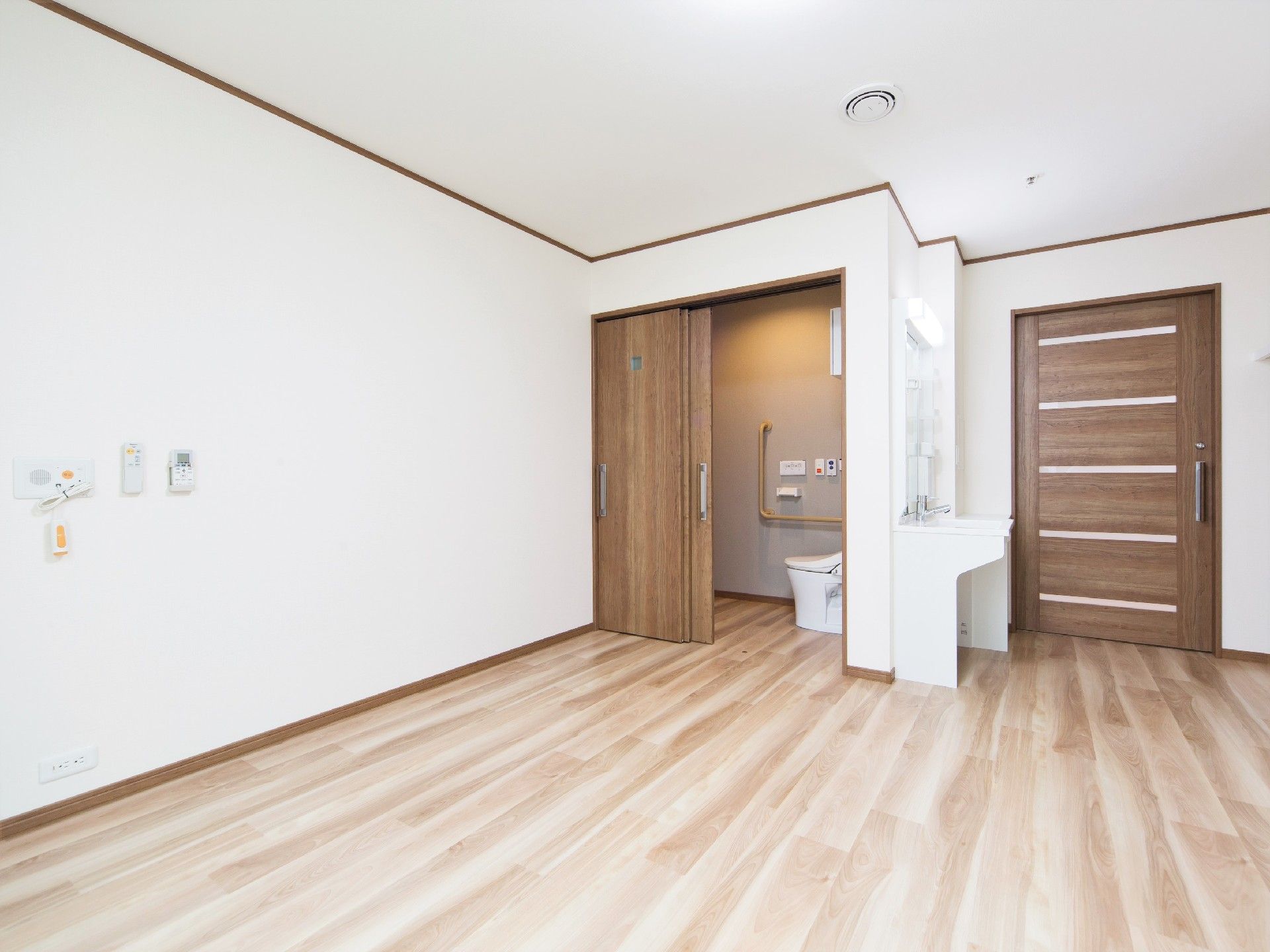 明るい色のフローリングと白い壁紙が温かい雰囲気。トイレと洗面所が付いた部屋。