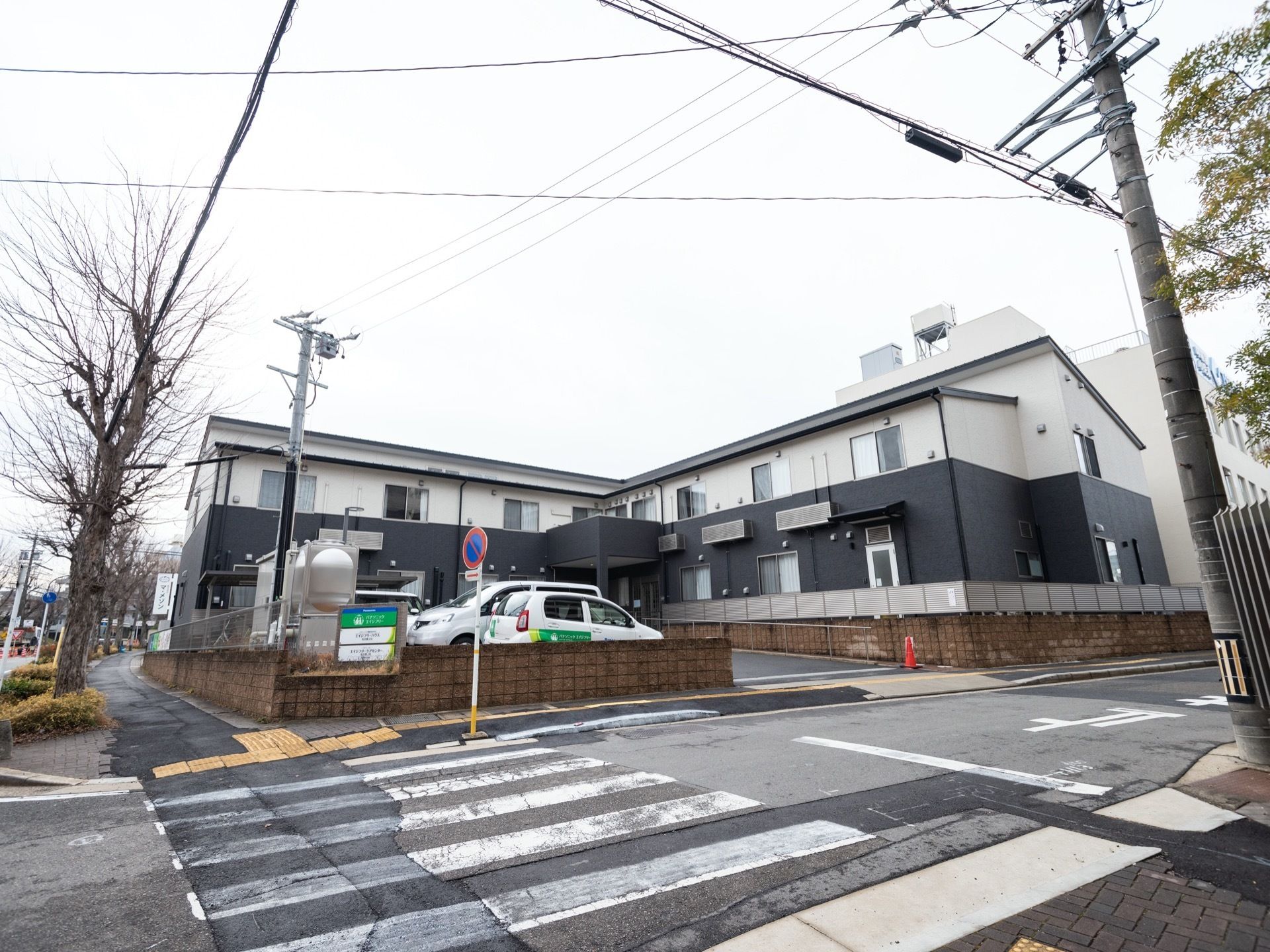 2階建てで白と濃い灰色のツートンカラーの建物。建物前に駐車場が設けられている。
