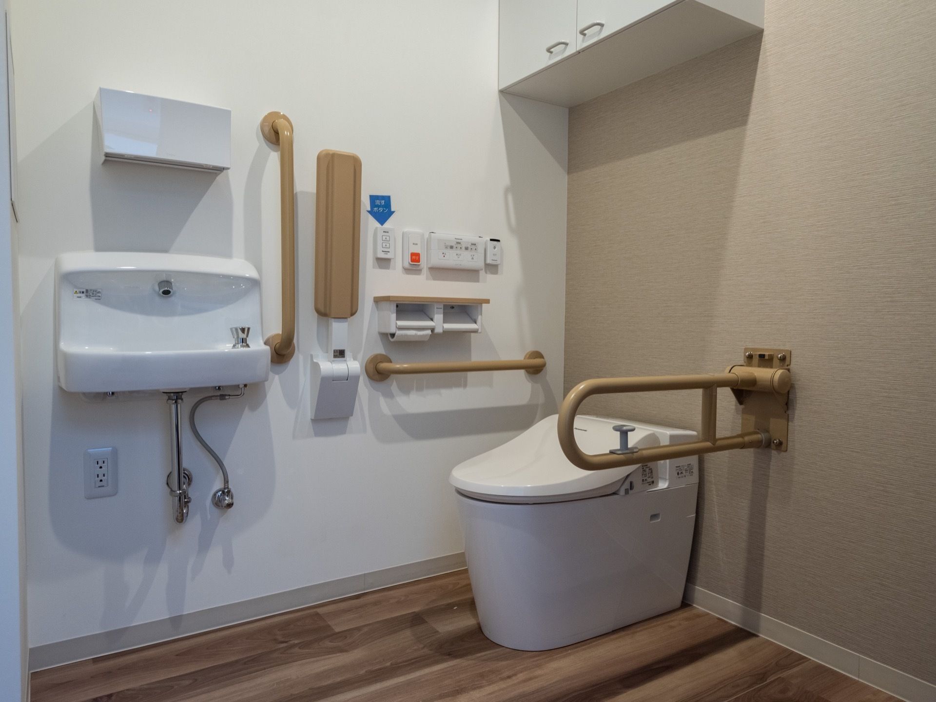 白を基調とした清潔感のるトイレとなっている。壁には複数の手すりが取付けられているほか、リモコンやペーパーホルダーもある。