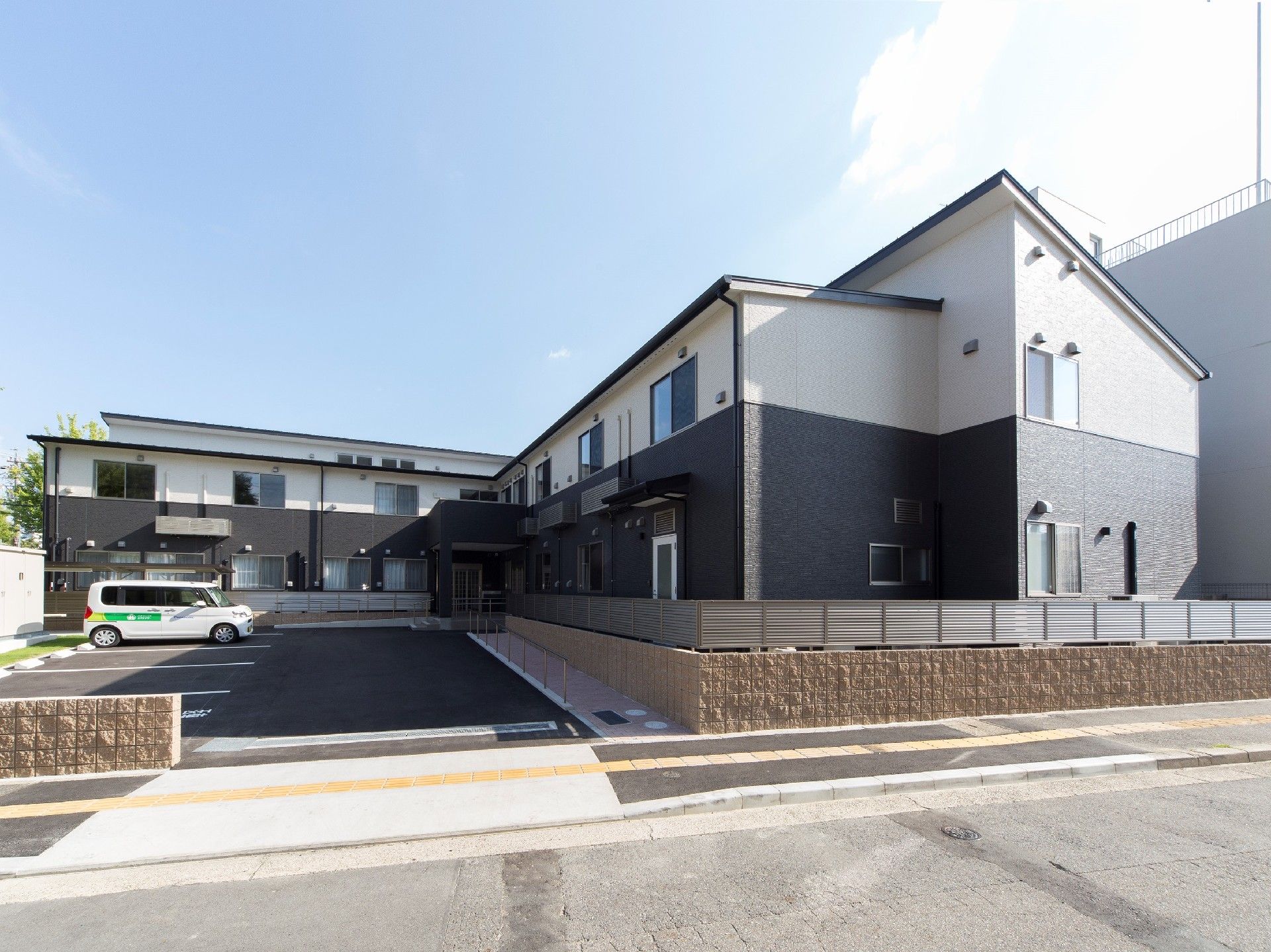 2階建てのエル字型の建物。中央に駐車スペースがあり、白い車が一台止まっている。