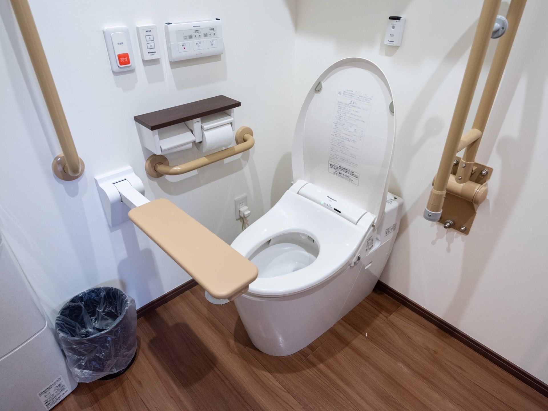 居室のトイレは白色と木目調のデザインというデザインである。温水洗浄便座で、周囲には複数の手すりがついている。