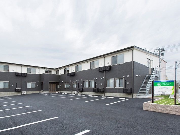 2階建ての建物の前には駐車場があり、建物の横には看板が立ち、アットホームな雰囲気。