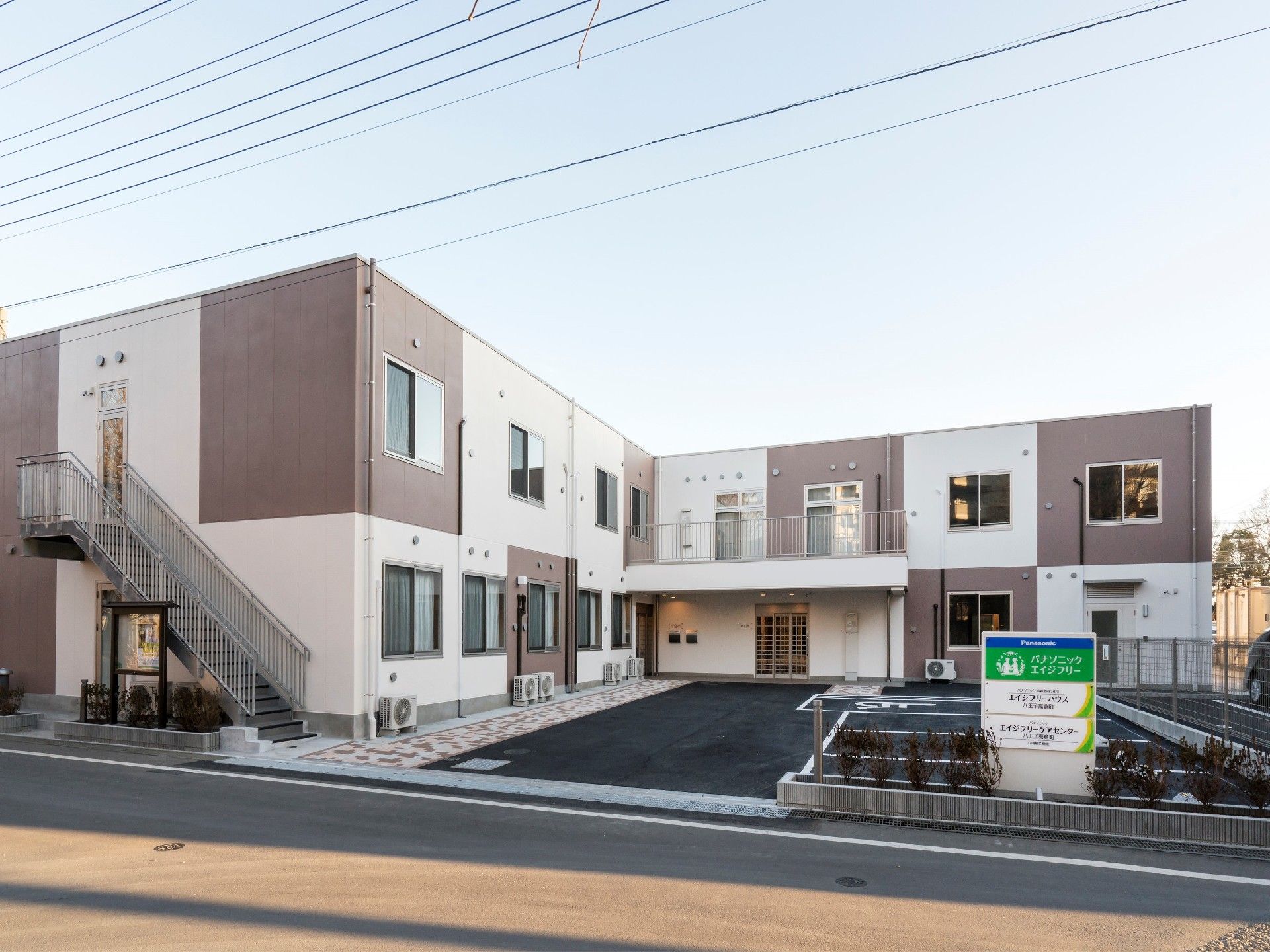 屋外階段が付いた建物は2階建てでシンプルなデザインで駐車スペースもある。