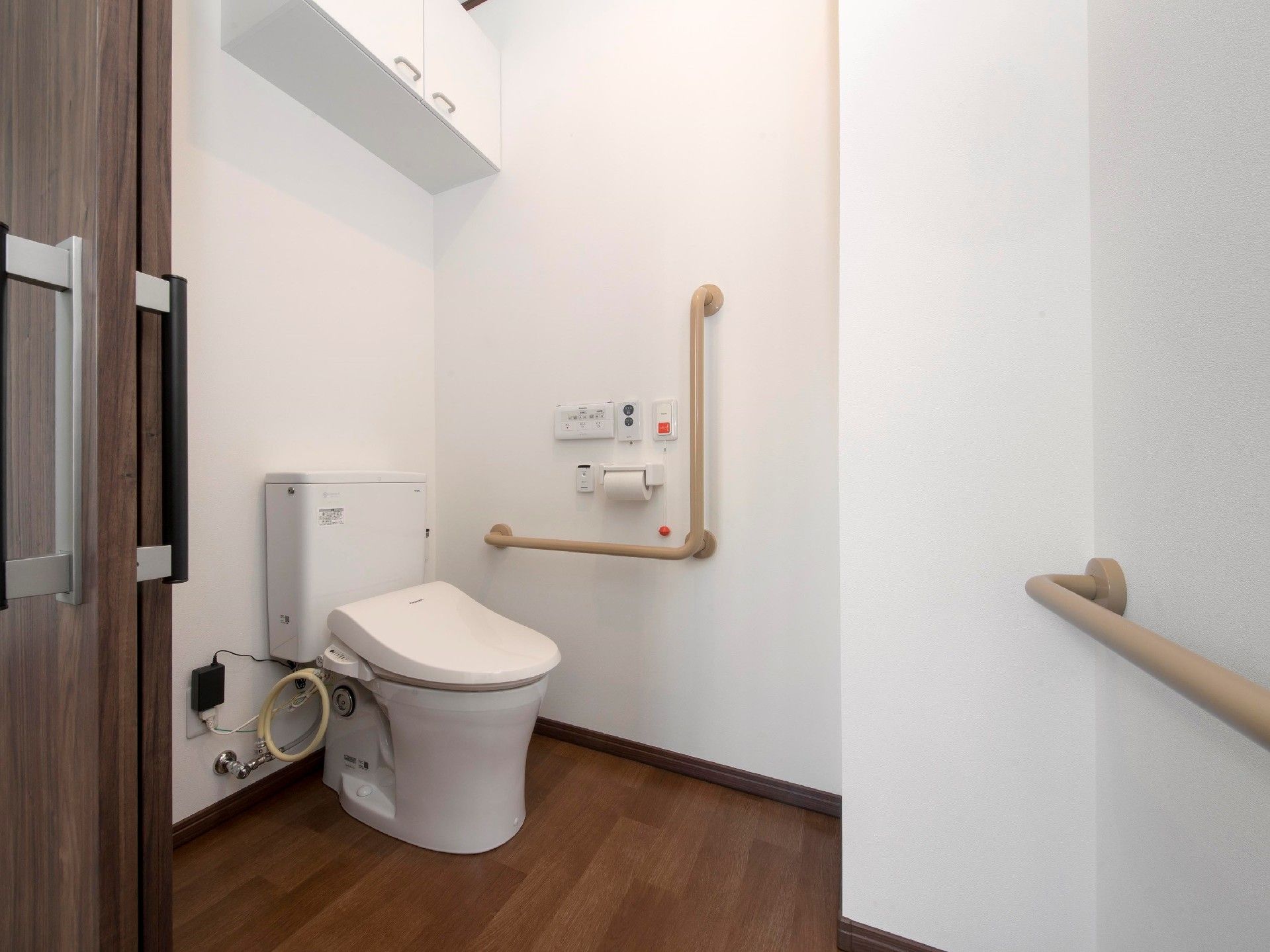 引き戸が付いたトイレは広く、壁にはエル字型の手すりや呼び出しボタンが付いている。