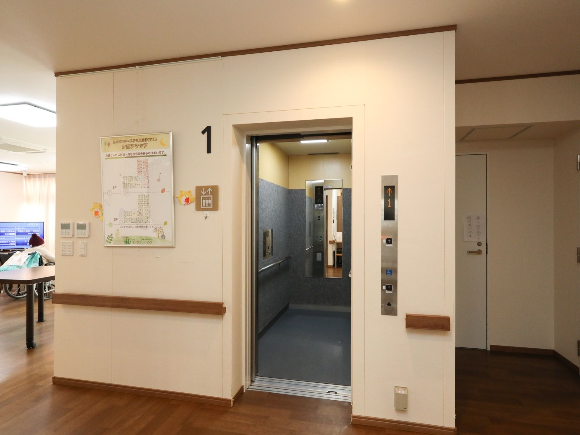エレベーターの入口付近や内部には手すりが設けられている。壁には館内案内図が貼られている。床はフローリングになっている。