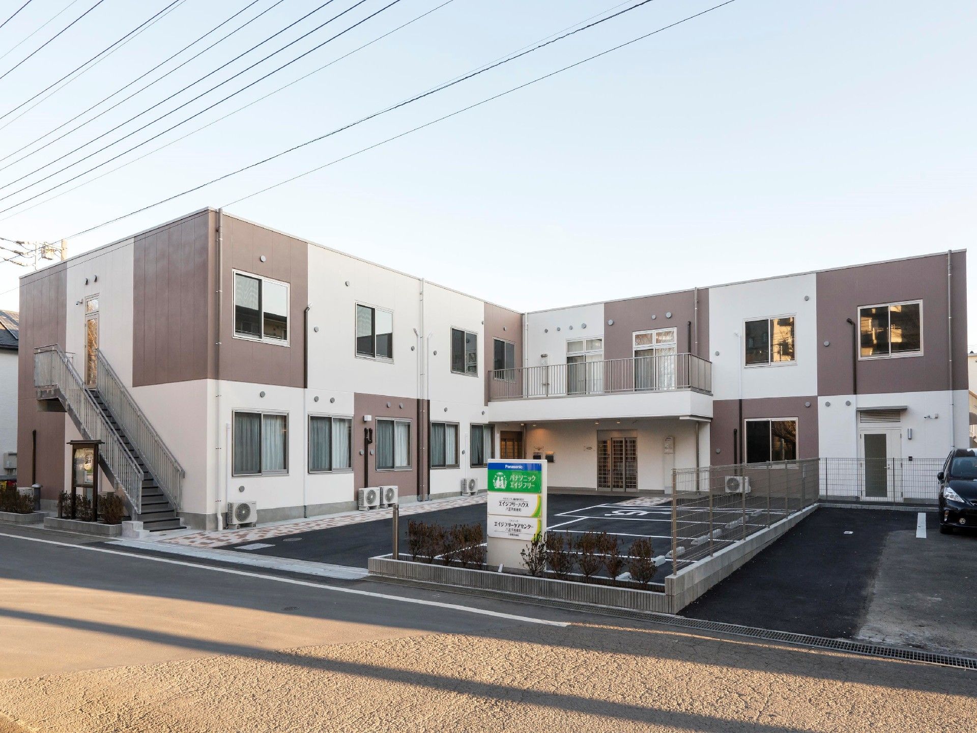 2階建ての建物。ブラウンとベージュのモザイク模様で、広い駐車場もある。