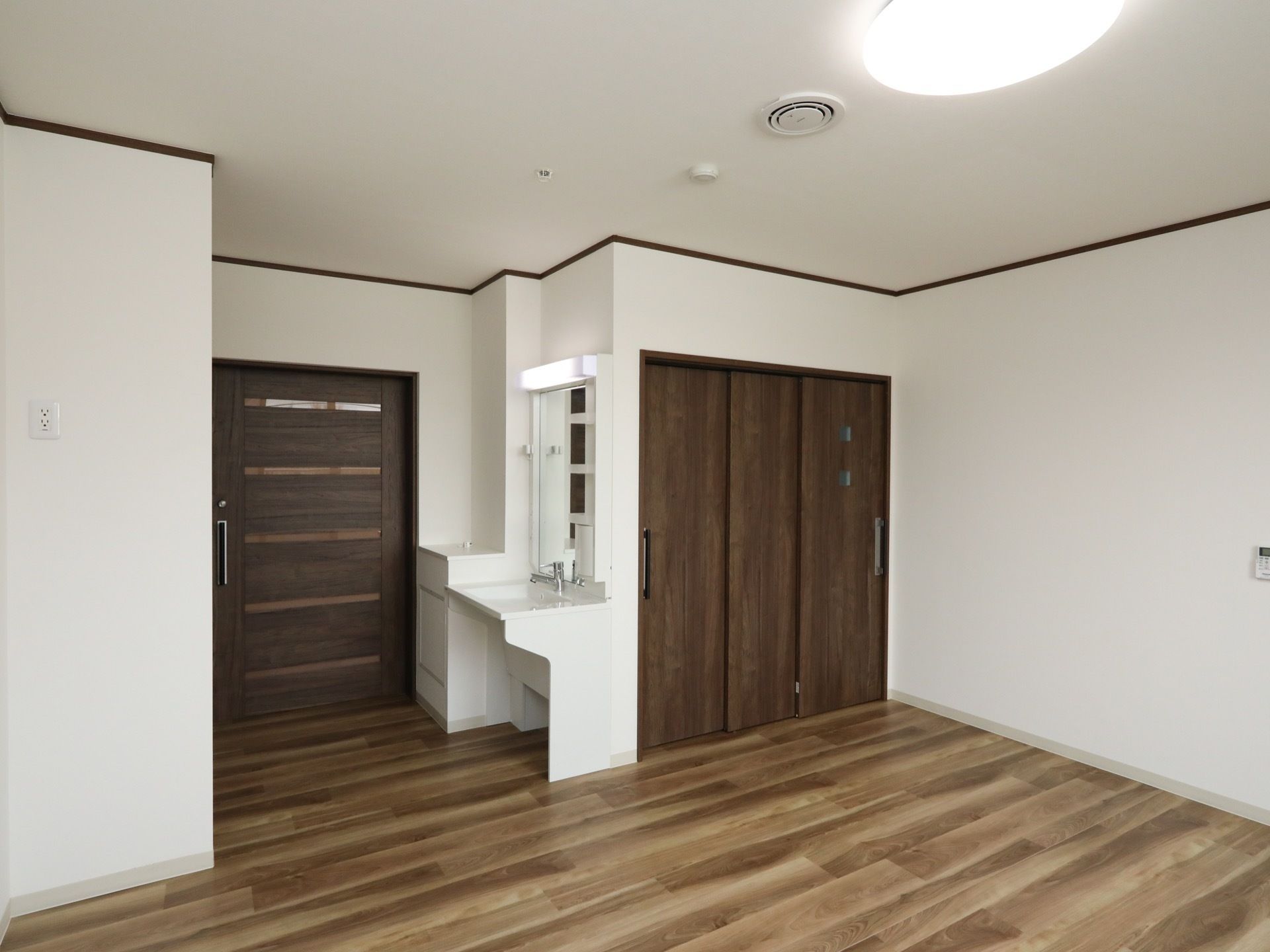 フローリングが敷かれた居室がある。洗面台が設置されており、入り口やトイレは木目調の引き戸で仕切られている。