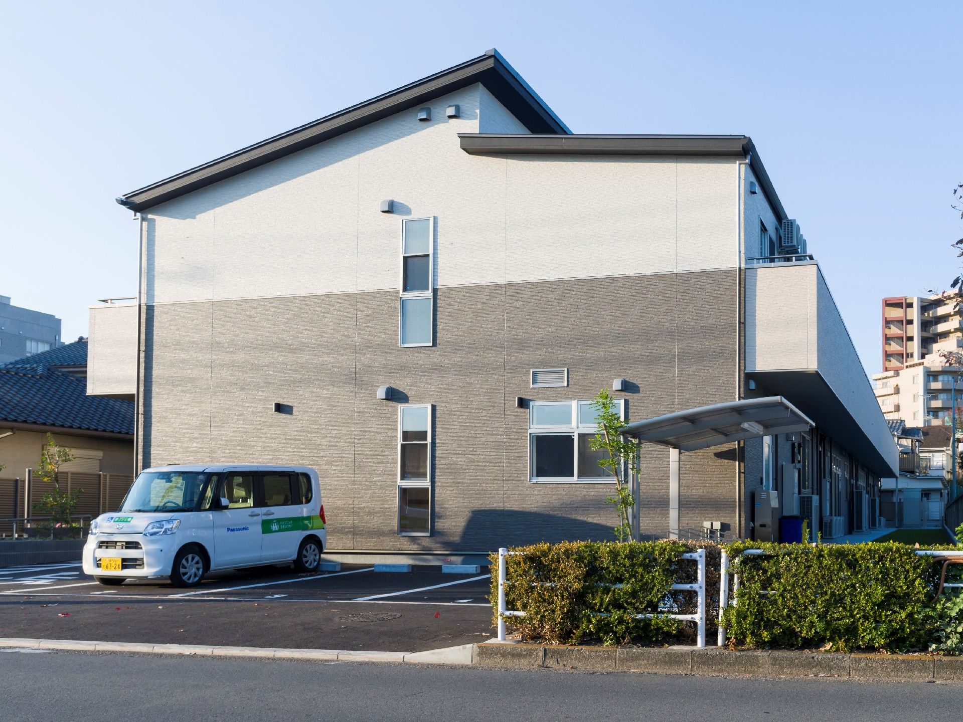 2階建ての建物。1階部分はダークグレー、2階部分は白で、周辺には住宅がある。